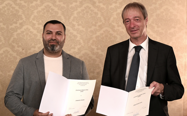 Alaaeddin Alhalabi und Rudolf Vouk bei der Preisverleihung. Beide halten die Urkunden in der Hand und lächeln in die Kamera. 